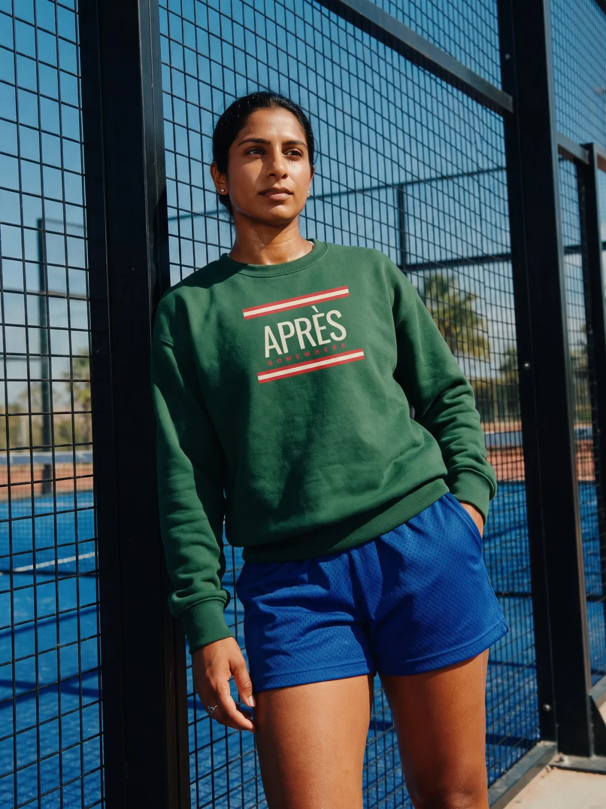 A woman on a padel court in a green APRÈS crewneck