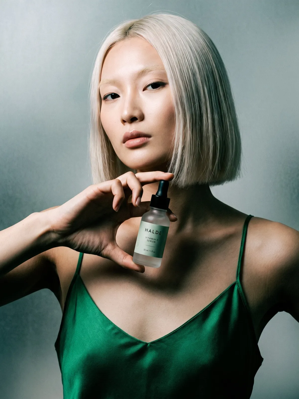 A model holds a HALDE serum bottle at her collarbone